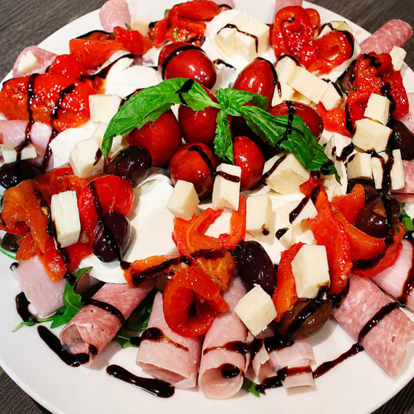 Close-up of an antipasto platter with meats, cheeses, roasted peppers, tomatoes, olives, and basil.