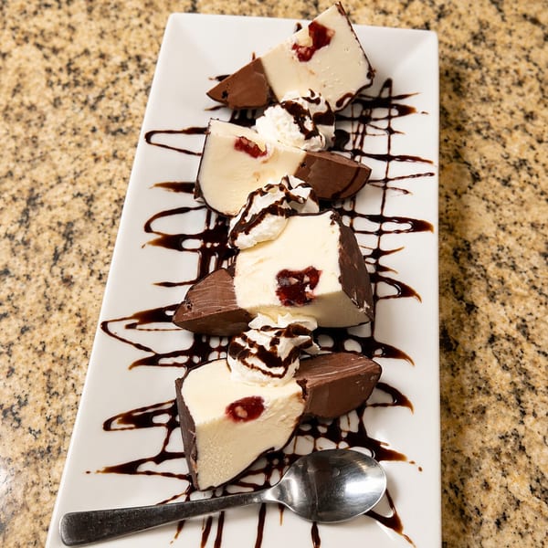 White chocolate cherry dessert slices with whipped cream and chocolate drizzle on a white plate.