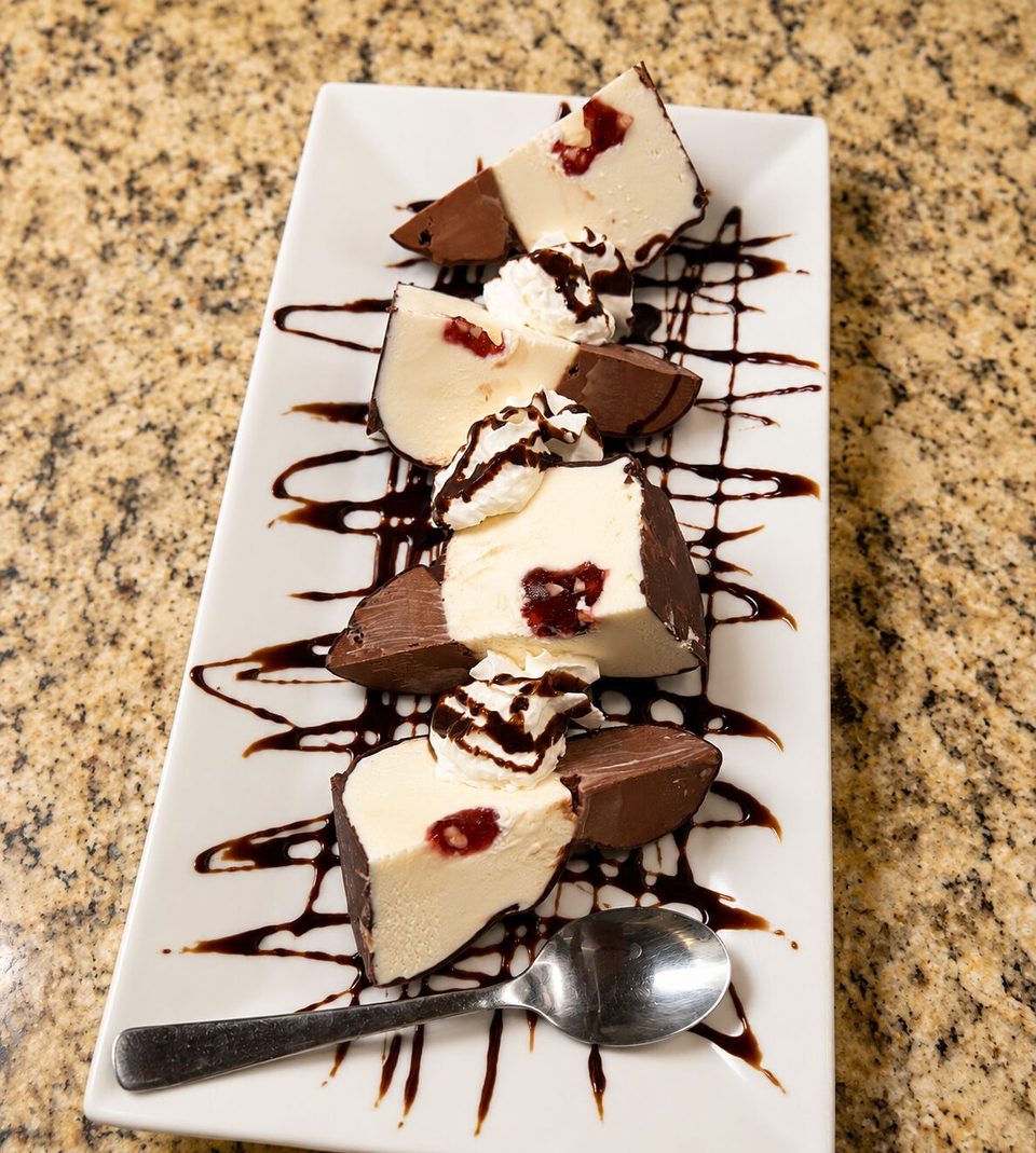 White chocolate cherry dessert slices with whipped cream and chocolate drizzle on a white plate.