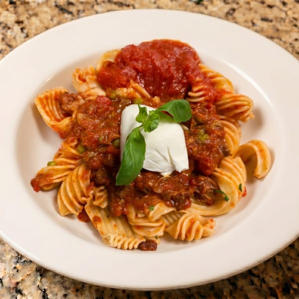 Pasta with red sauce, a dollop of burrata cheese, and basil on a white plate.