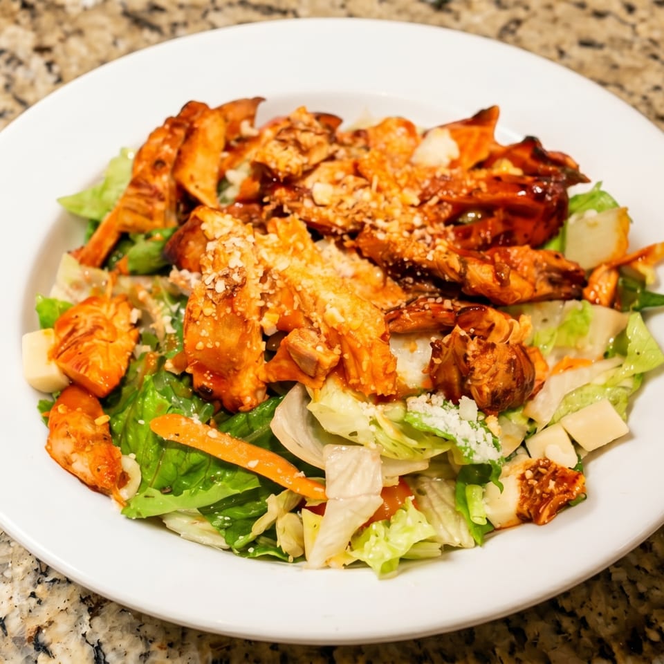 A white plate holds a salad with grilled chicken, lettuce, carrots, and parmesan cheese.