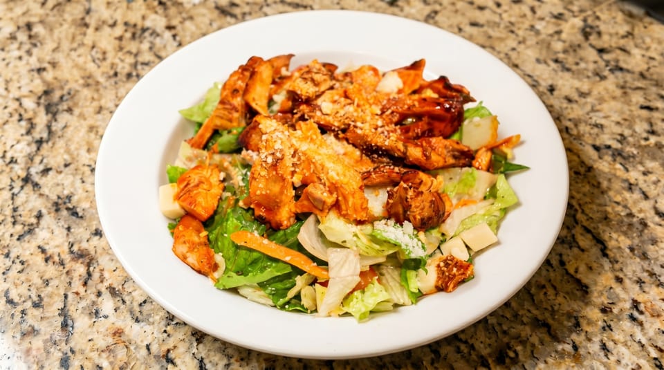 A white plate holds a salad with grilled chicken, lettuce, carrots, and parmesan cheese.