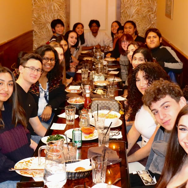A large group of young people smiling and posing for a photo at a long restaurant table.