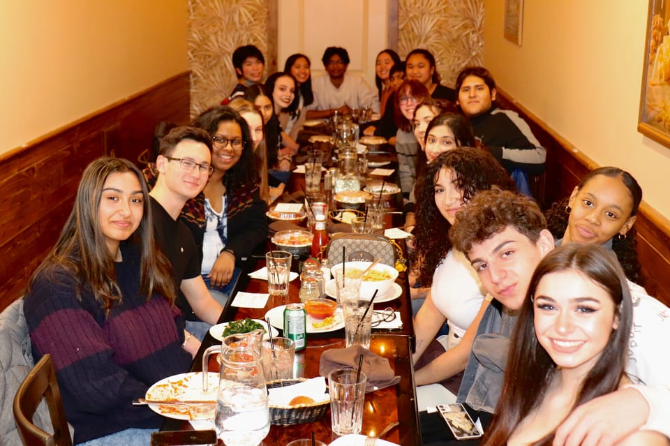 A large group of young people smiling and posing for a photo at a long restaurant table.