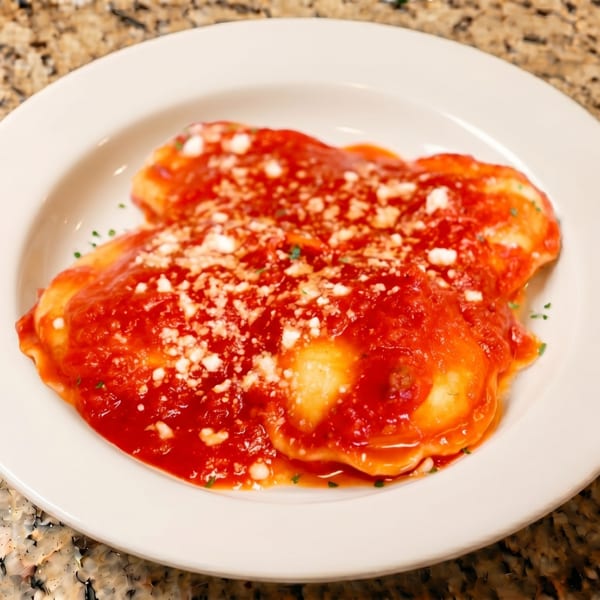 A white plate of ravioli covered in red sauce, sprinkled with white cheese and herbs.