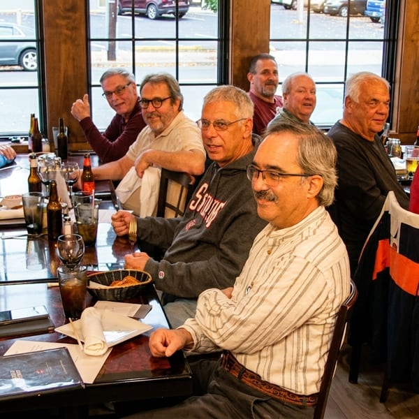 A group of men seated at a long table in a restaurant, with drinks and menus.