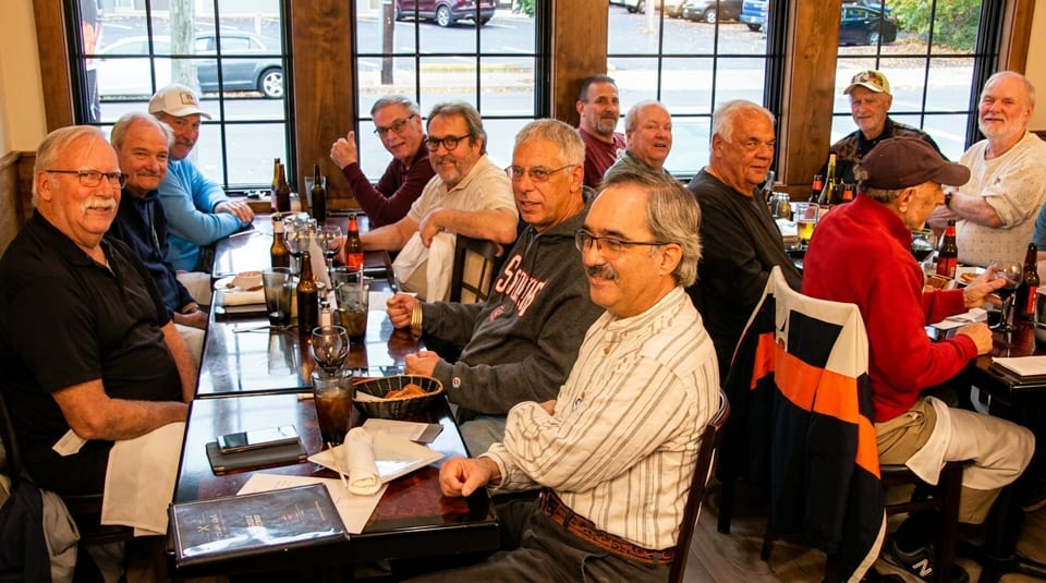A group of men seated at a long table in a restaurant, with drinks and menus.