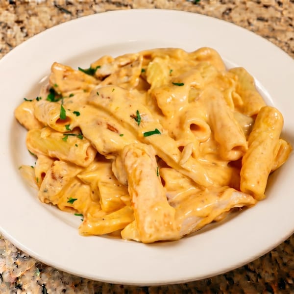 Creamy rigatoni pasta with chicken and parsley on a white plate, on a granite countertop.