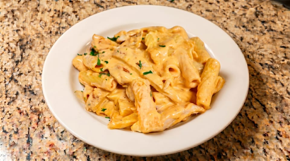 Creamy rigatoni pasta with chicken and parsley on a white plate, on a granite countertop.