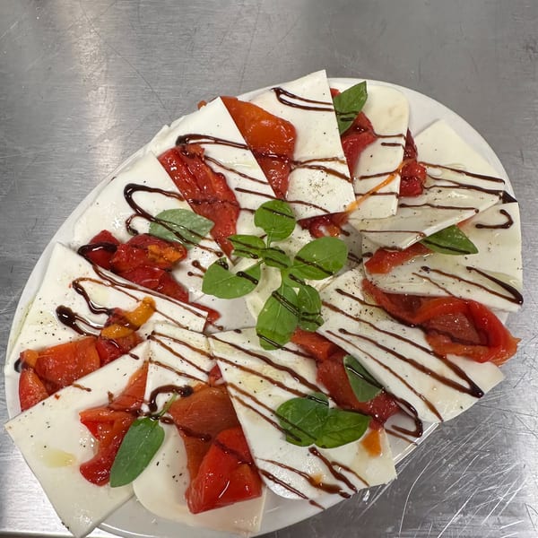 A white platter of mozzarella slices, roasted red peppers, basil, and balsamic glaze.