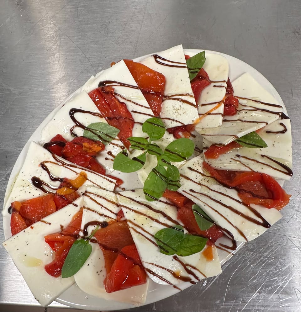 A white platter of mozzarella slices, roasted red peppers, basil, and balsamic glaze.