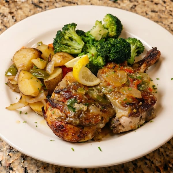 Grilled chicken with lemon, roasted potatoes, onions, peppers, and broccoli on a white plate.