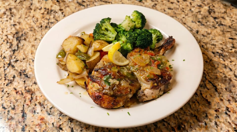 Grilled chicken with lemon, roasted potatoes, onions, peppers, and broccoli on a white plate.
