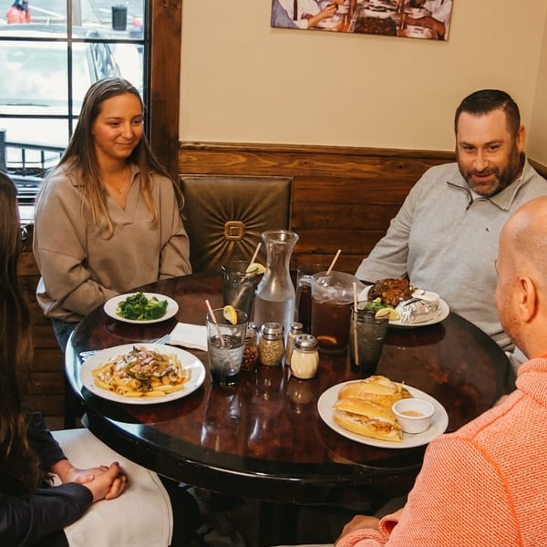 Four people enjoying various dishes and drinks at a round table in a cozy restaurant.