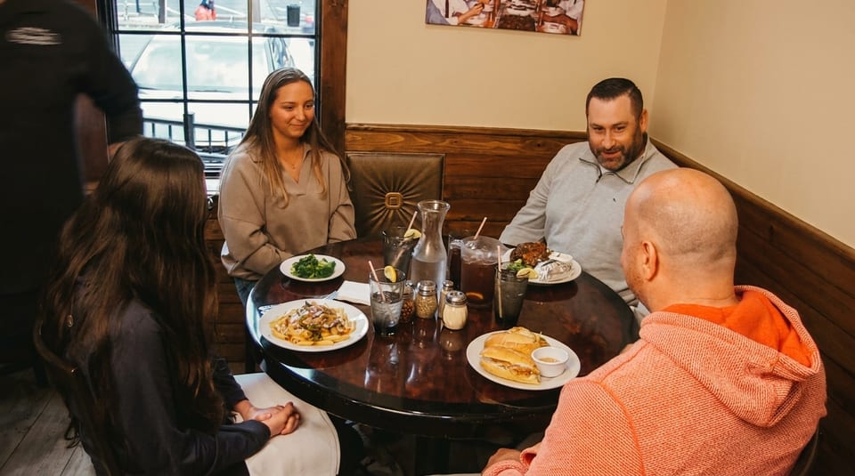 Four people enjoying various dishes and drinks at a round table in a cozy restaurant.
