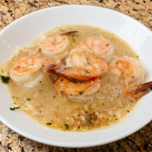A white bowl filled with shrimp scampi in a creamy sauce, garnished with herbs.