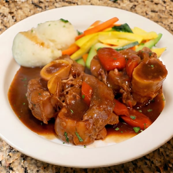 Braised meat with gravy, mashed potatoes, and mixed vegetables on a white plate.