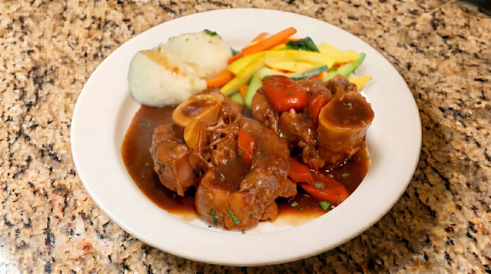 Braised meat with gravy, mashed potatoes, and mixed vegetables on a white plate.