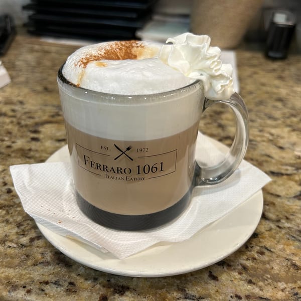 Ferraro 1061 Italian Eatery branded mug with a frothy latte, whipped cream, and cinnamon.