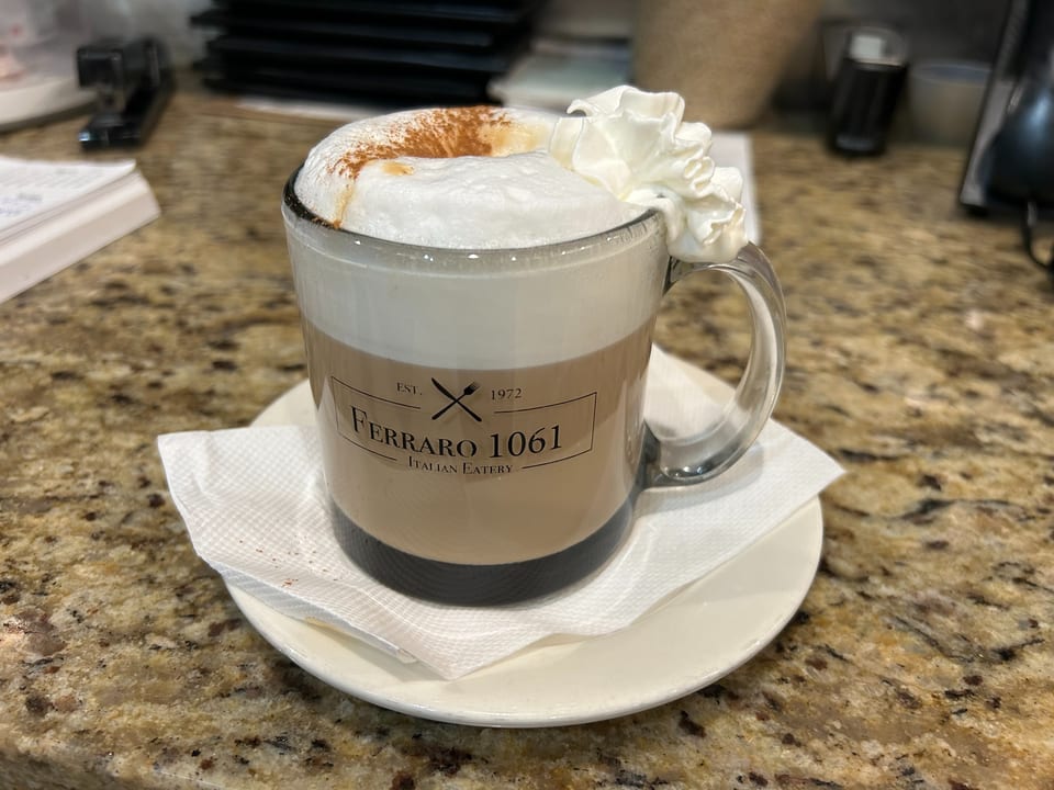 Ferraro 1061 Italian Eatery branded mug with a frothy latte, whipped cream, and cinnamon.