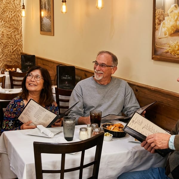 A server smiles while taking orders from three happy customers at a restaurant table.